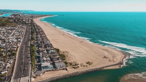 Vue aérienne d’une ville côtière, avec une longue plage, un quartier résidentiel dense et un océan bleu limpide.