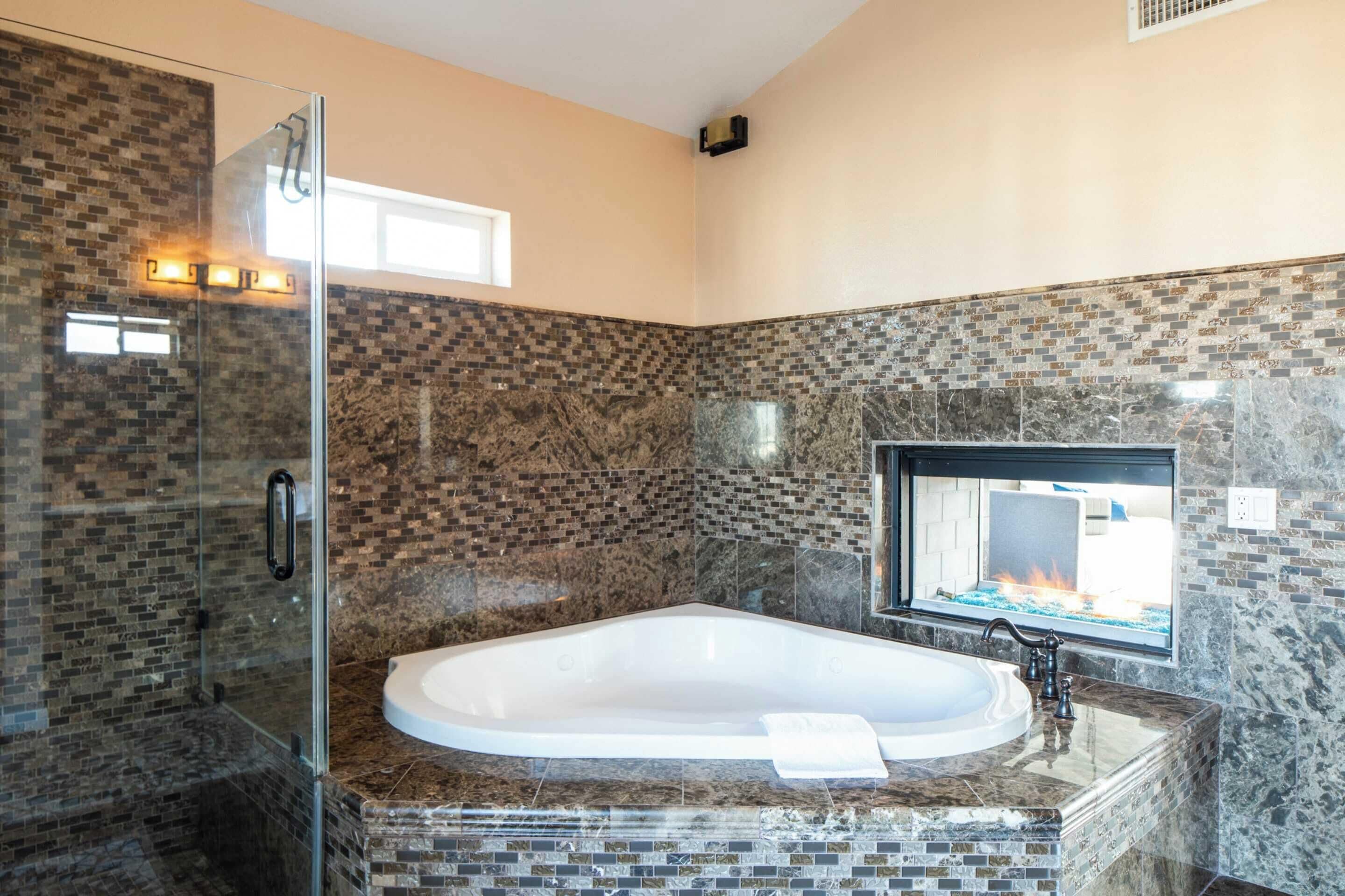 A modern bathroom with a glass-enclosed shower, a freestanding bathtub, and a large window with a view of a fire.