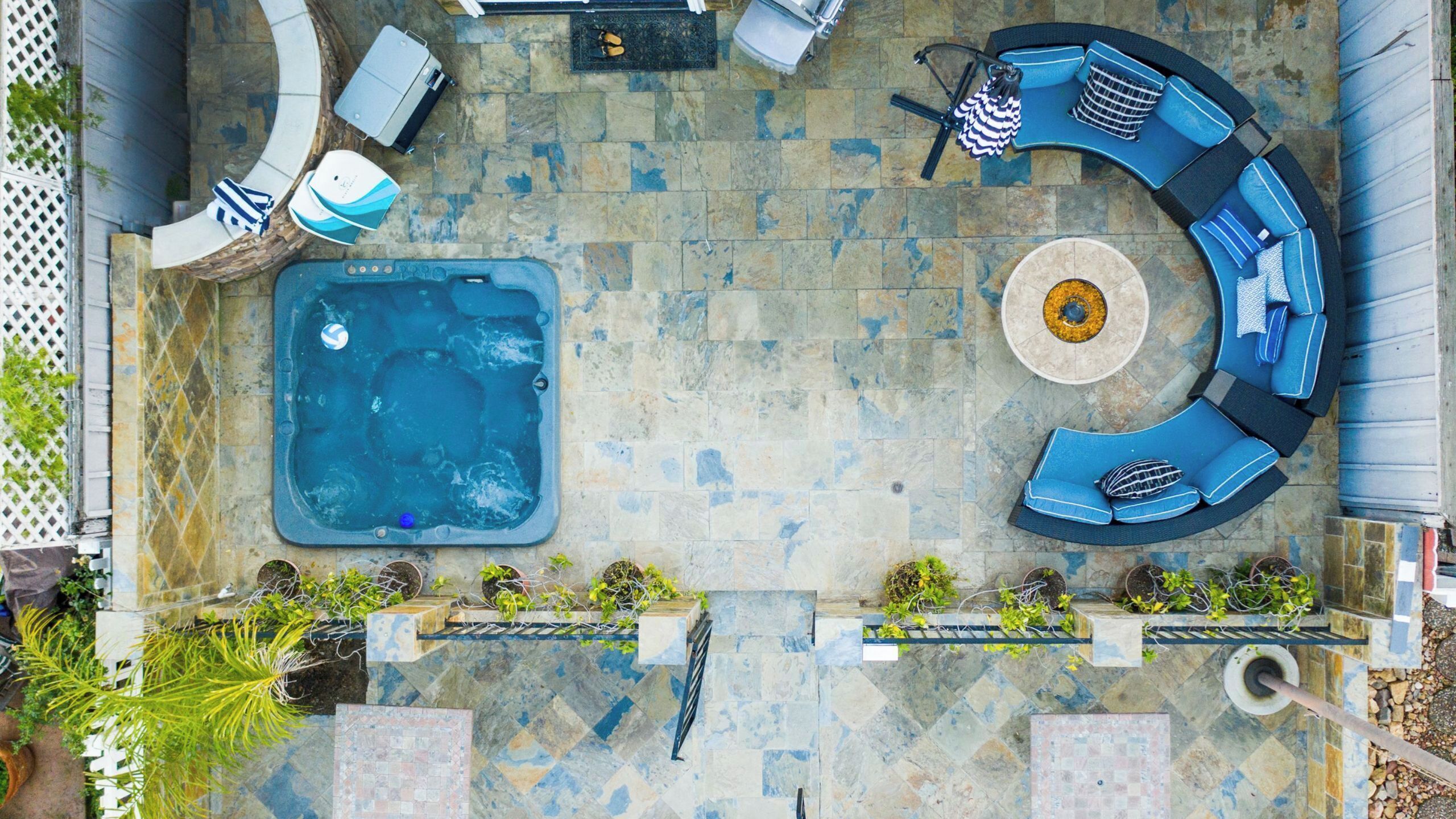 A rooftop patio with a hot tub, seating area, and potted plants.