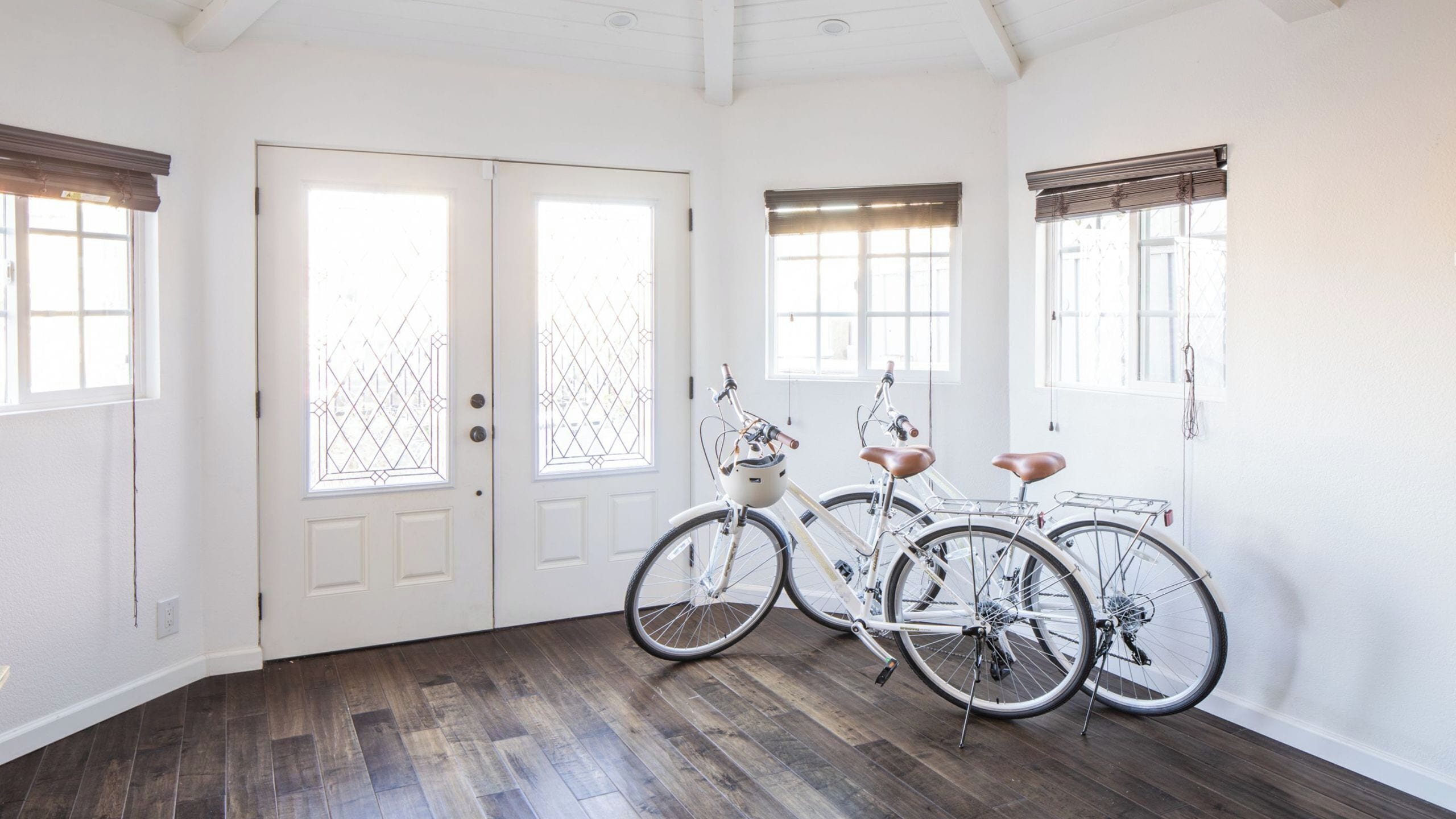 A room with a wooden floor, white walls, two doors with glass panels, and two bicycles parked against the wall.