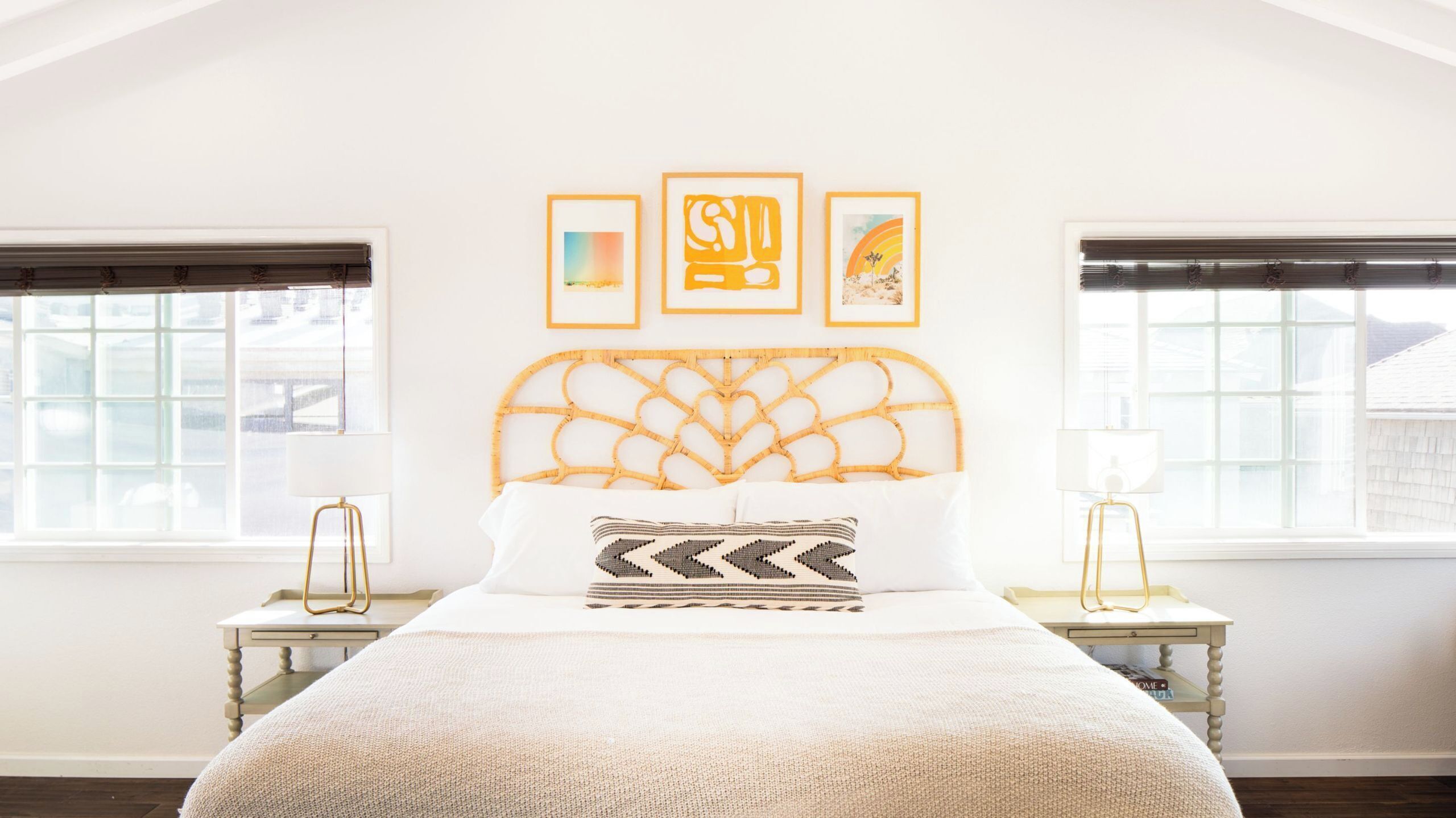 A bedroom with a bed, two nightstands, a window, and three framed artworks on the wall.