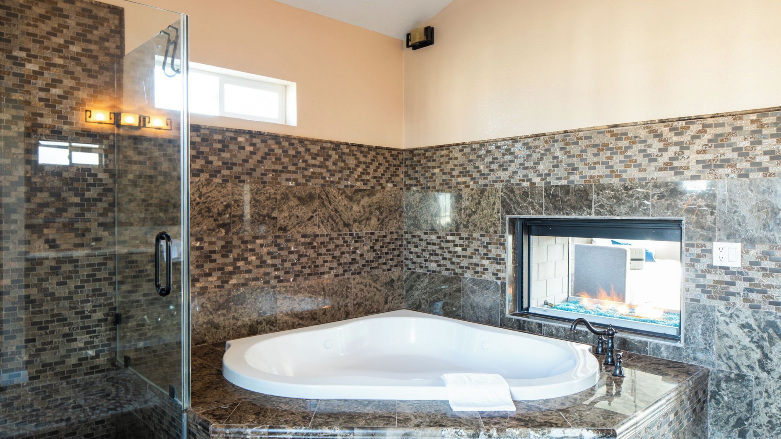 Ein Badezimmer mit Duschkabine aus Glas, freistehender Badewanne und einer mit Fliesen versehenen Wand mit Kamin.