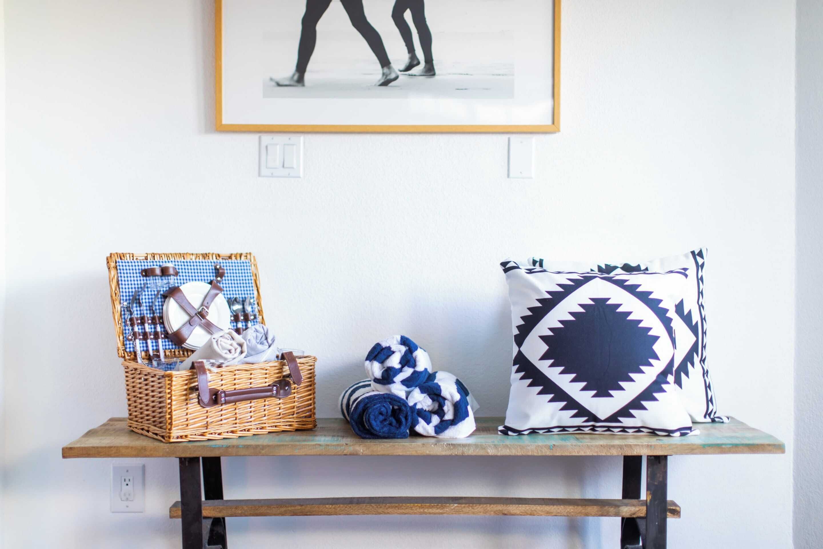 A wicker basket with towels and a pillow on a wooden table.