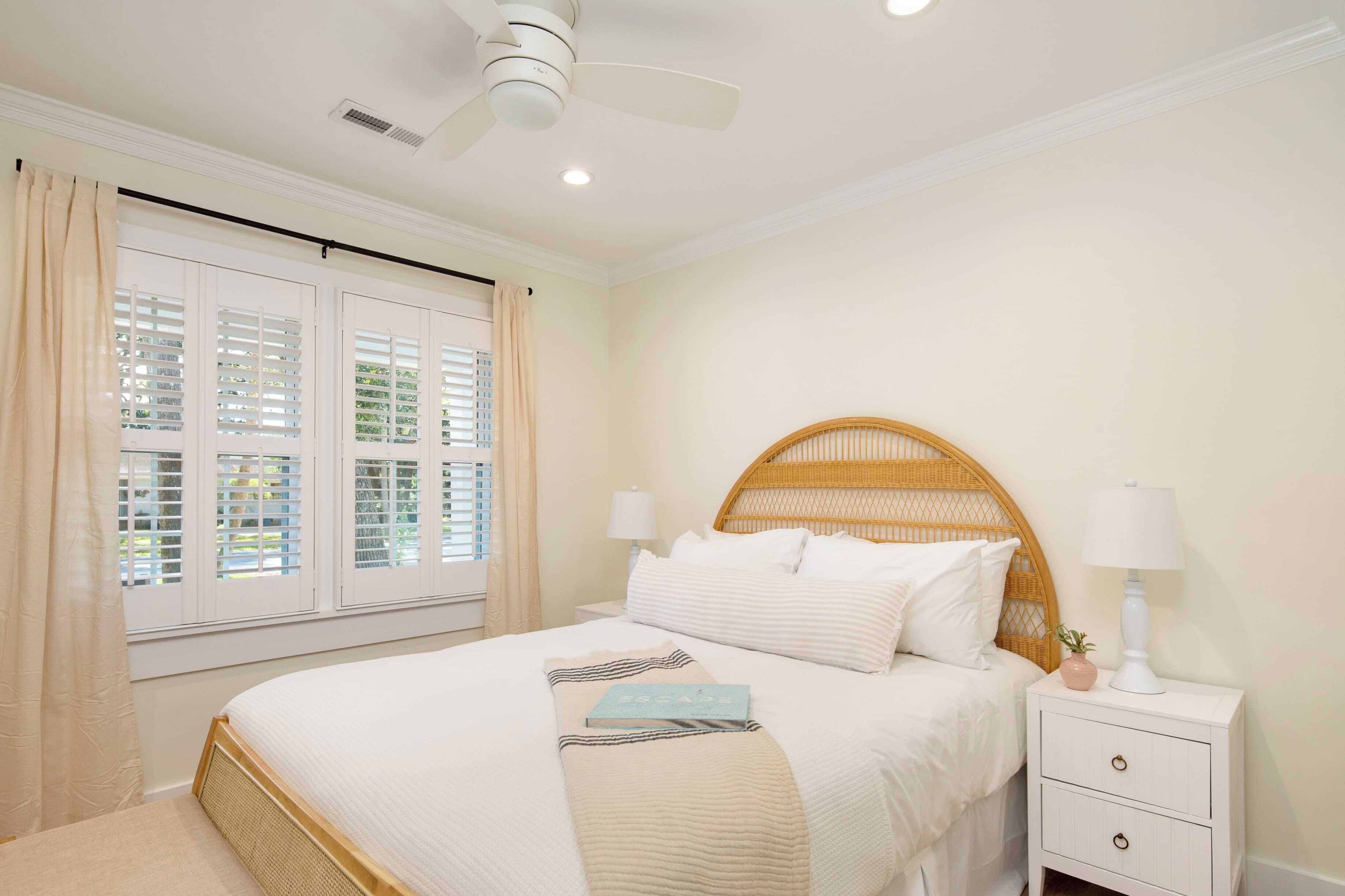 Quarto com cama, mesa de cabeceira, luminária, ventoinha no teto e janela com persianas.