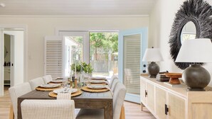 A dining area with a wooden table set for four, surrounded by wicker chairs, a rattan cabinet, and a large mirror. - Sawyer by Avantstay Stunning Isle Of Palms Home w/ Pool! (Isle of Palms)