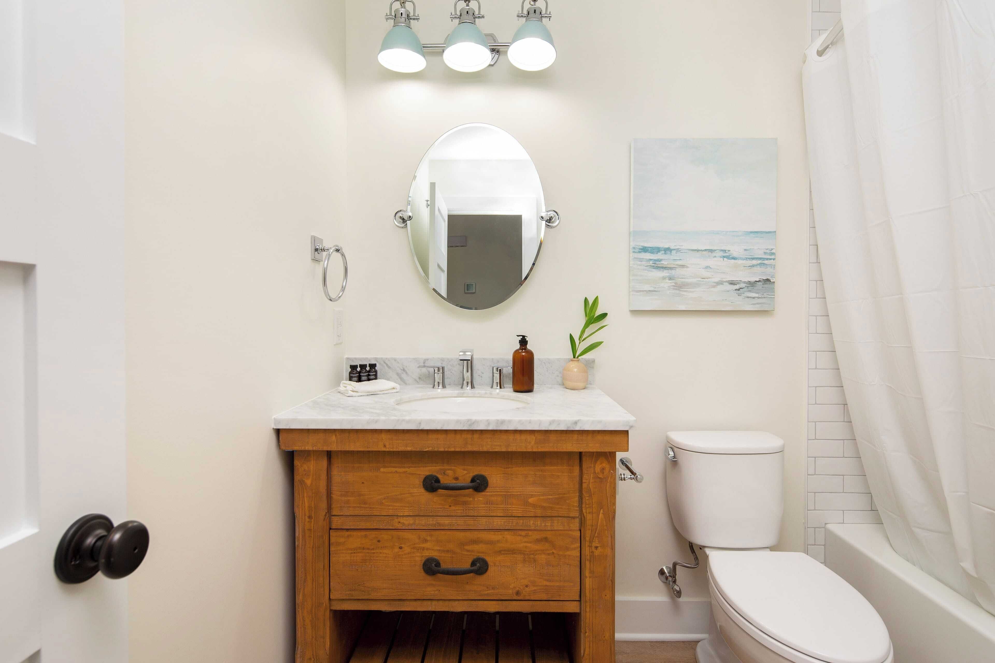 A bathroom with a wooden vanity, a white toilet, a bathtub, and a mirror with lights above.