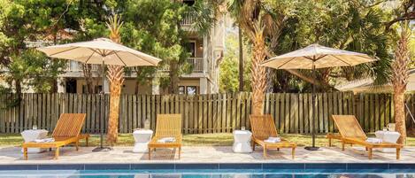 Un espace aménagé au bord de la piscine, avec des chaises longues en bois, des parasols et une clôture en bois en arrière-plan.