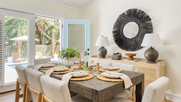 A dining area with a wooden table set for four, surrounded by chairs, a large mirror, and two wall-mounted lamps. - Sawyer by Avantstay Stunning Isle Of Palms Home w/ Pool! (Isle of Palms)