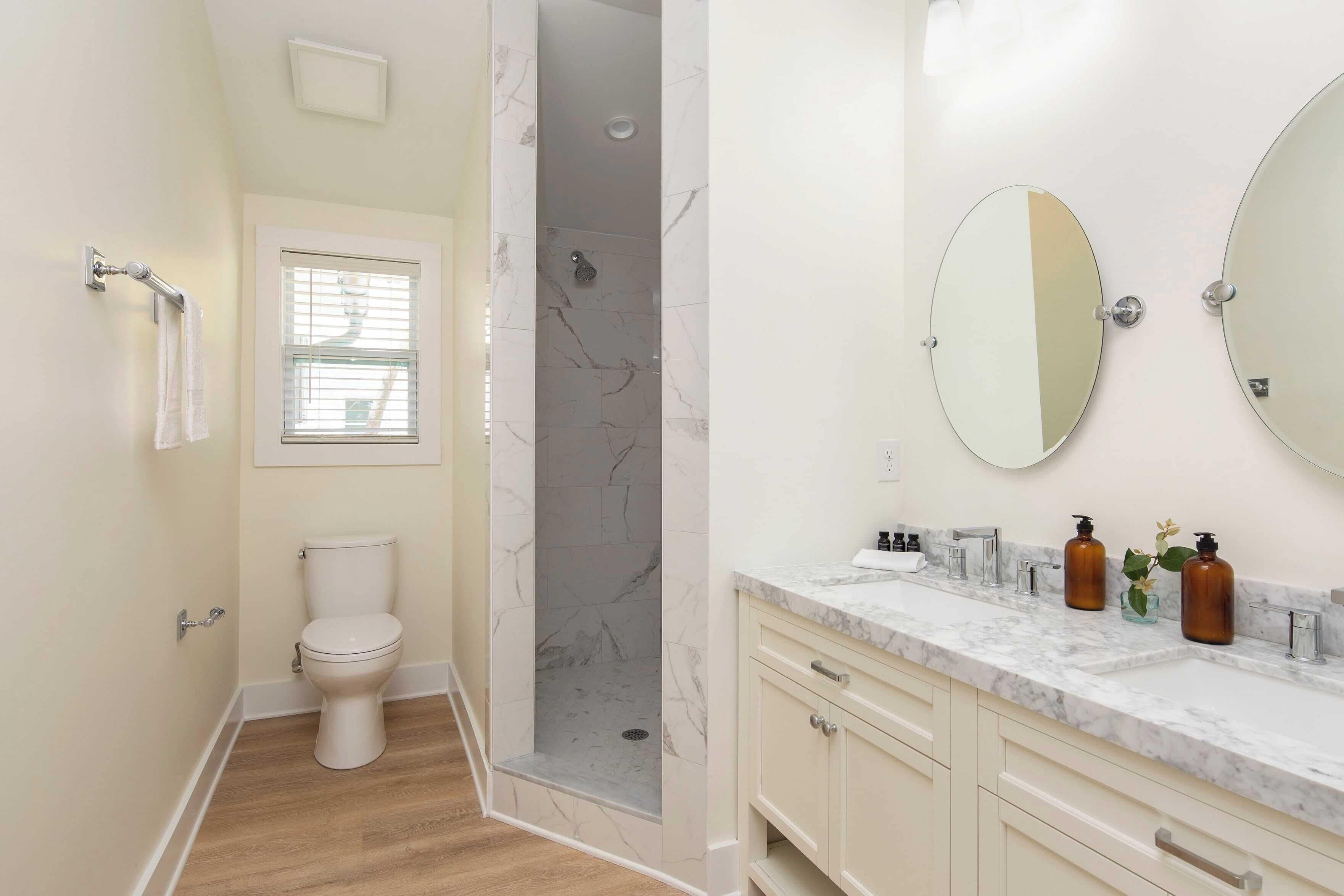 A bathroom with a toilet, a shower with marble walls, a vanity with a sink, and two mirrors.