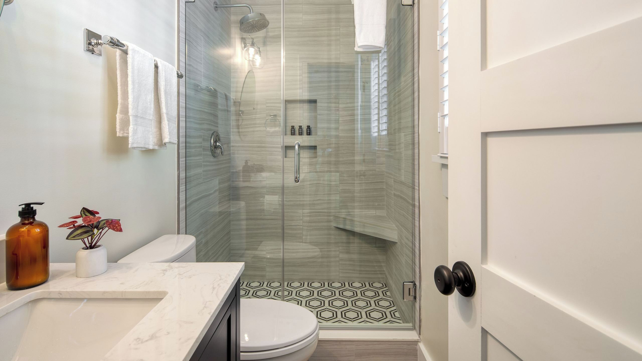 A modern bathroom with a glass-enclosed shower, a toilet, a sink with a marble countertop, and a potted plant.