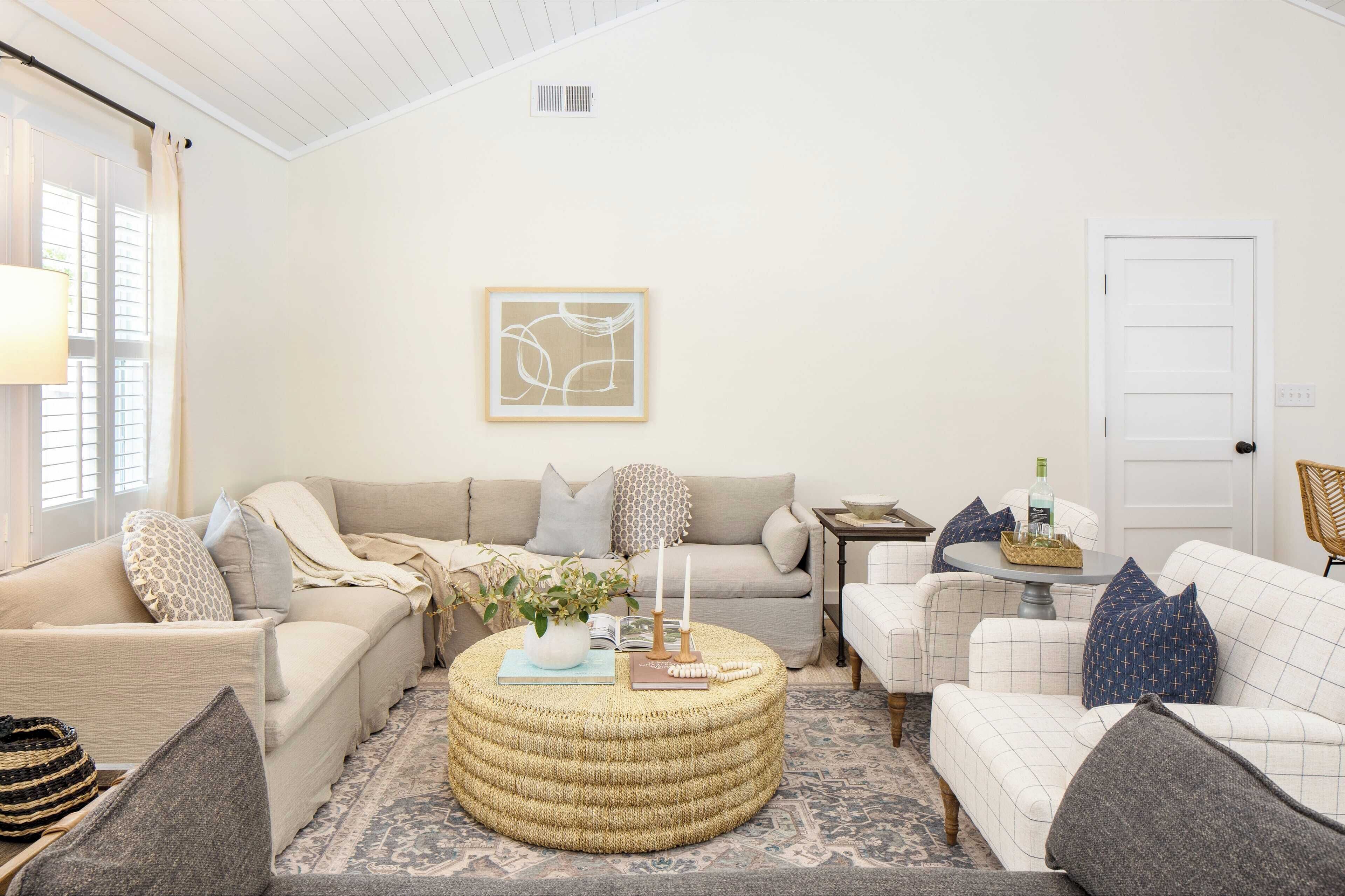 Ein gemütliches Wohnzimmer mit einem beigen Sofa, einem runden Hocker und einem kleinen Beistelltisch mit Kerzen.