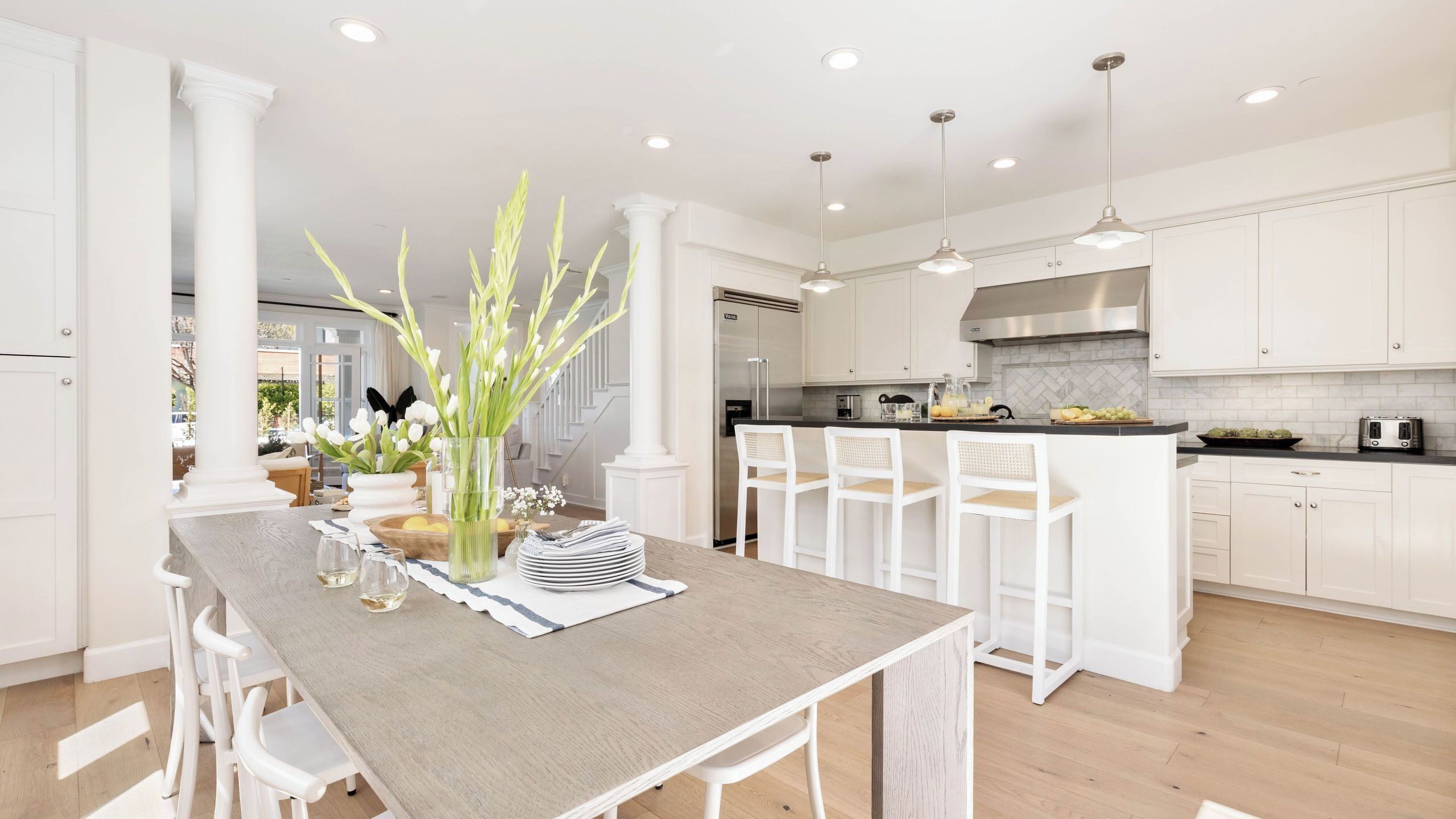 Una cocina moderna con armarios blancos, una isla central con sillas y una mesa de comedor para seis personas.