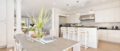Una cocina moderna con armarios blancos, una isla central con sillas y una mesa de comedor para seis personas.