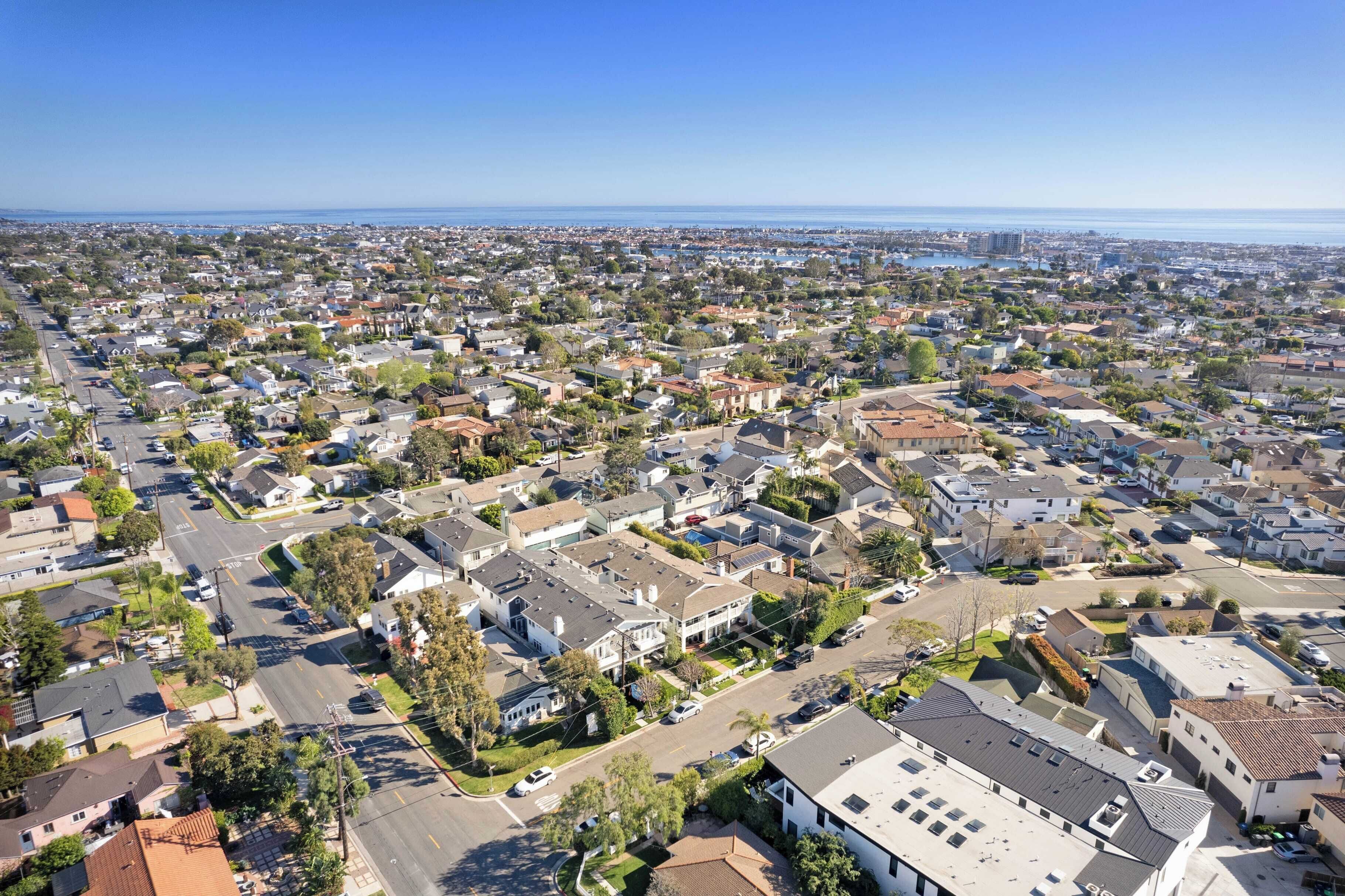 An aerial view of a residential area with houses, streets, and a clear view of the ocean.