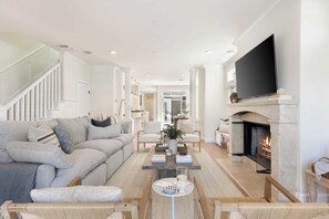 Een moderne woonkamer met een open haard, een grote flatscreen televisie en een comfortabele zithoek.