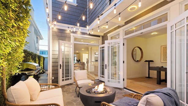 An outdoor patio with wicker furniture, a fire pit, and string lights. - Crystal Cove by Avantstay Gorgeous & Charming Newport Home! (Newport Beach)
