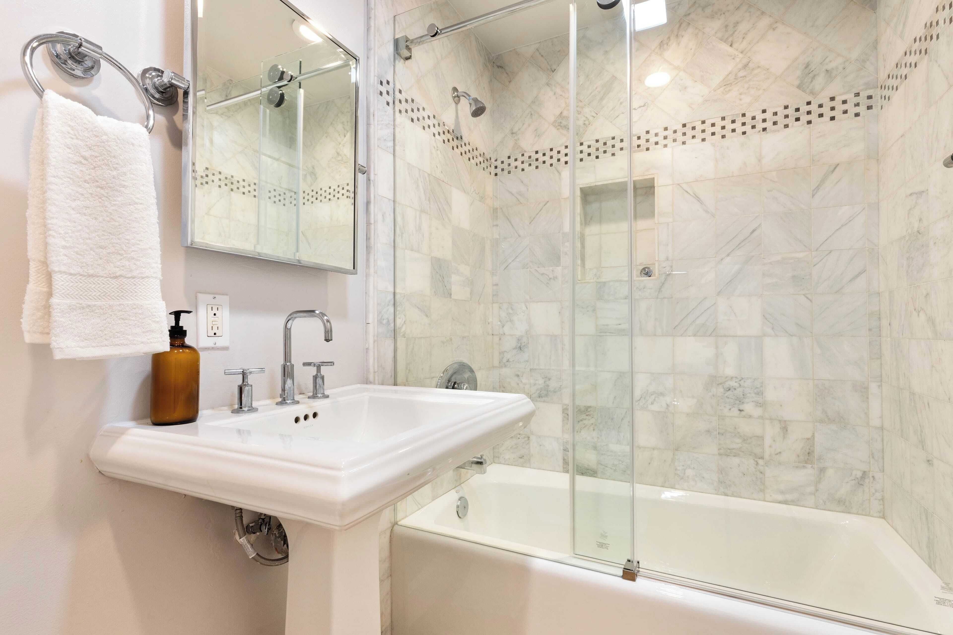 A modern bathroom with a white sink, a glass-enclosed shower, and a white bathtub.
