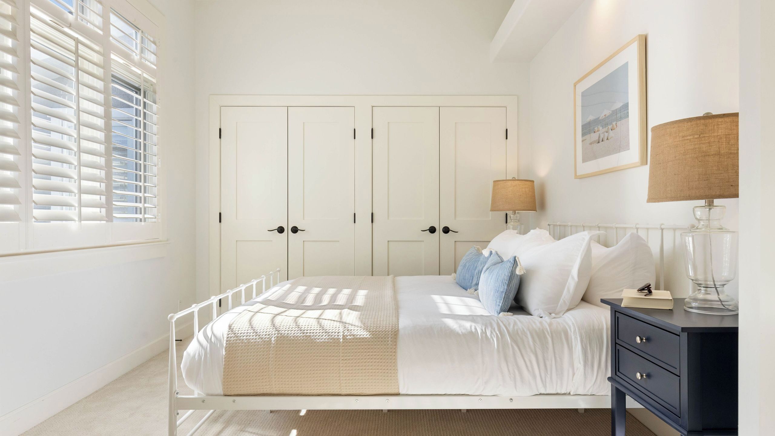 A bedroom with a bed, bedside table, lamp, and a window with blinds.