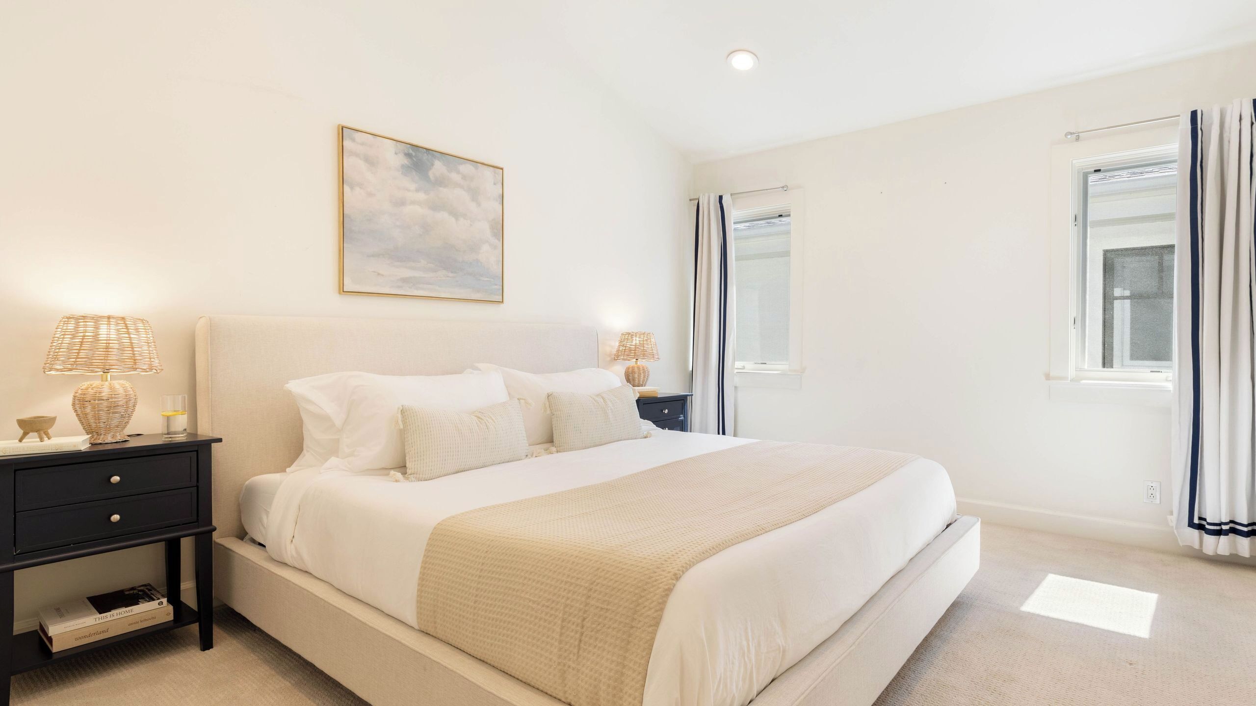 A bedroom with a bed, two bedside tables, a window, and a painting on the wall.