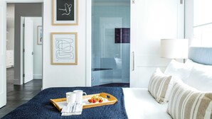 A hotel room with a bed, a tray with breakfast, framed artwork, and a sliding door to a bathroom. - O'neill I by Avantstay Coastal Paradise Steps From Beach Modern Decor (Newport Beach)