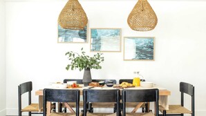 A dining area with a wooden table, black chairs, and woven pendant lights. There are framed pictures on the wall and a potted plant on the table. - O'neill I by Avantstay Coastal Paradise Steps From Beach Modern Decor (Newport Beach)