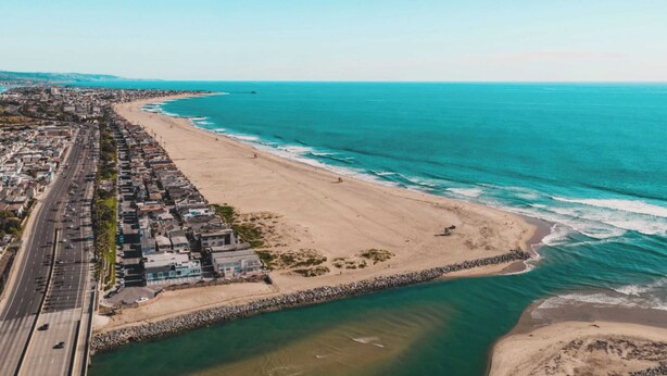 An aerial view of a coastal city with a long beach, a road parallel to the shore, and a small building near the beach. - O'neill I by Avantstay Coastal Paradise Steps From Beach Modern Decor (Newport Beach)