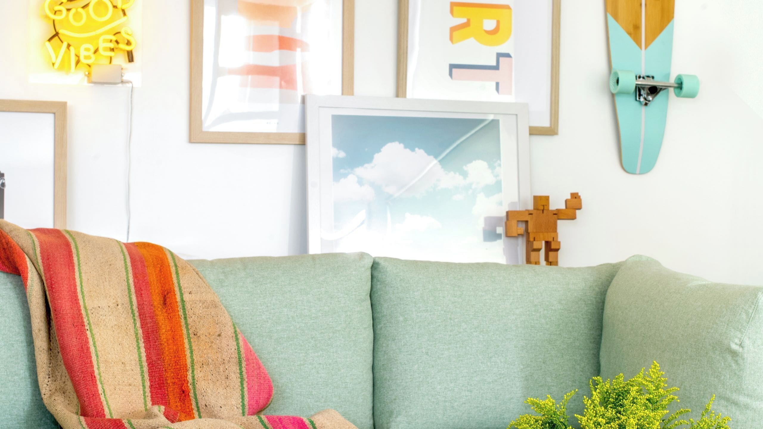 Ein Zimmer mit einer grünen Couch, einer bunten Decke, gerahmten Kunstwerken und einem Skateboard.