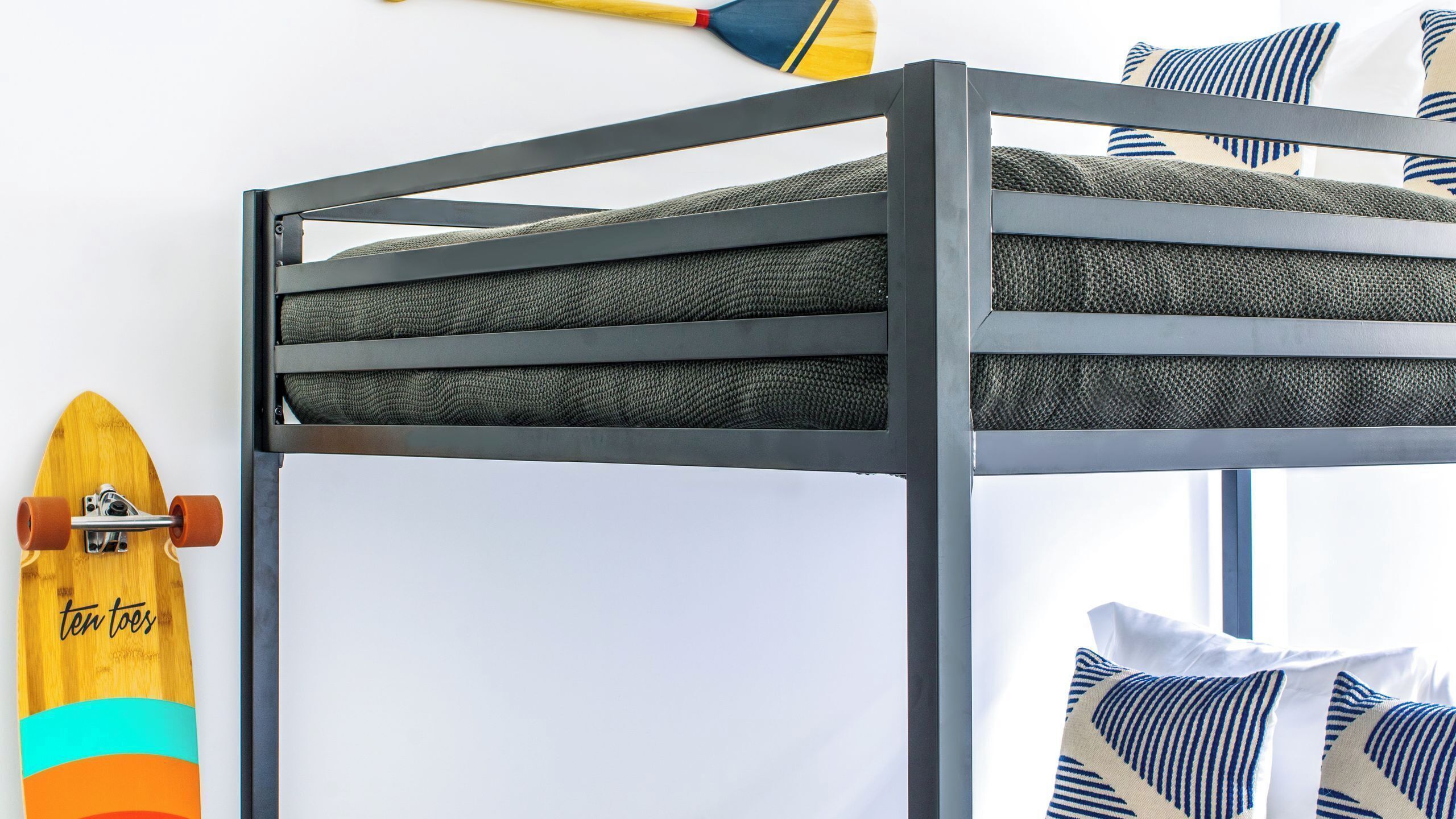 Een stapelbed met een skateboard tegen de muur, een borstel en gestreepte kussens.