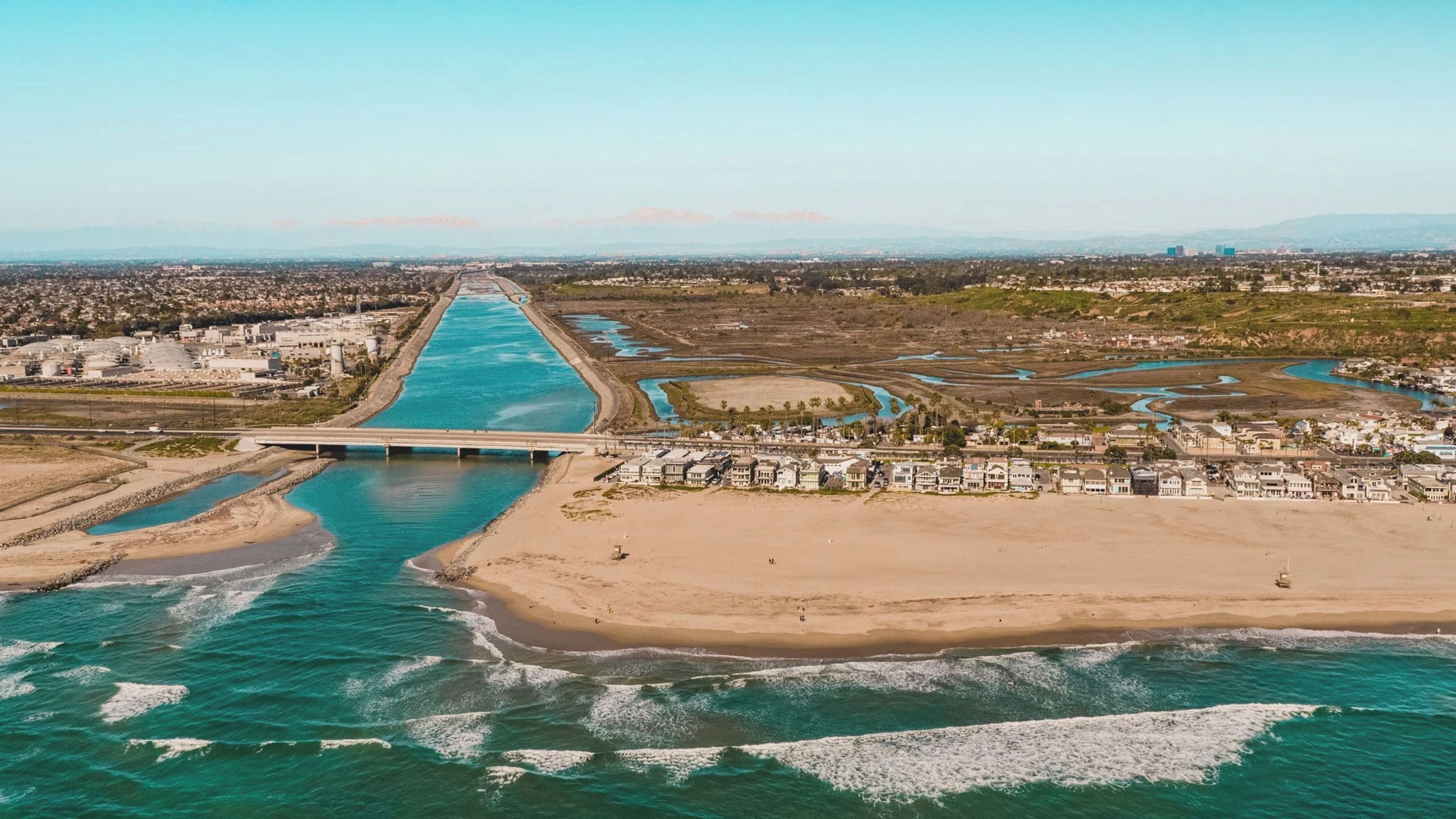 Vista aérea de una zona costera con un puente, playa y edificios residenciales.