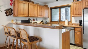 A kitchen with wooden cabinets, a central island with bar stools, a dishwasher, and a refrigerator. - Riverside Condos B101 by Avantstay Condo Close To Downtown, Town Park & Ski Lift #8 (Telluride)