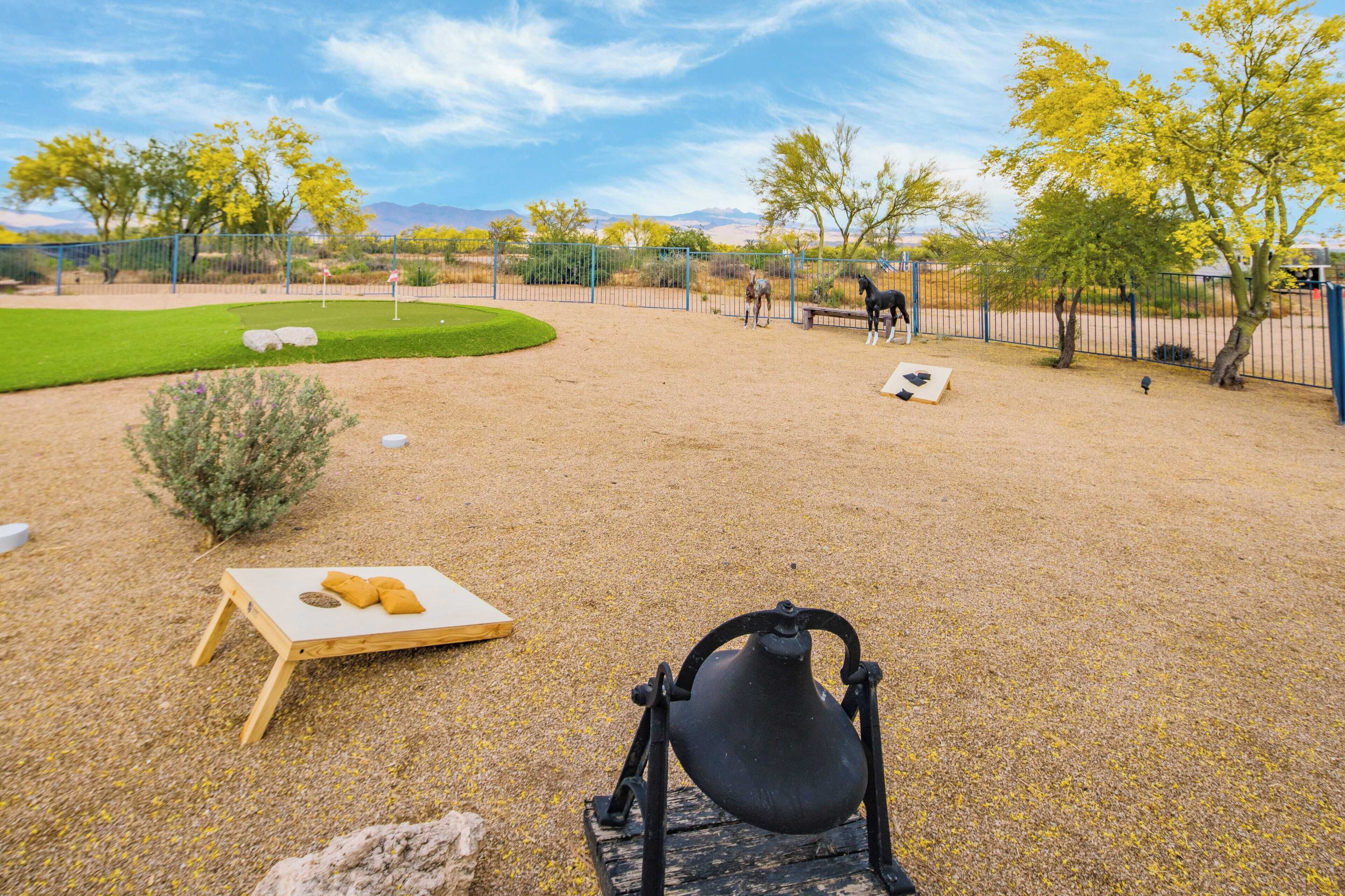 A fenced outdoor area with a horse, a wooden table with a cushion, and a bell.