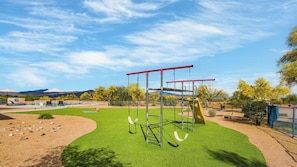A playground with swings and a climbing structure, surrounded by a fenced area with a pool and lounge chairs. - Fallbrook by Avantstay Secluded Home on 40acres W/pool, Rooftop & Trails! (Scottsdale)