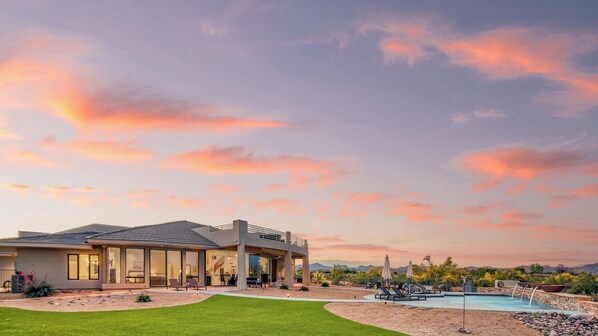A modern house with a swimming pool, outdoor seating, and a view of mountains.
