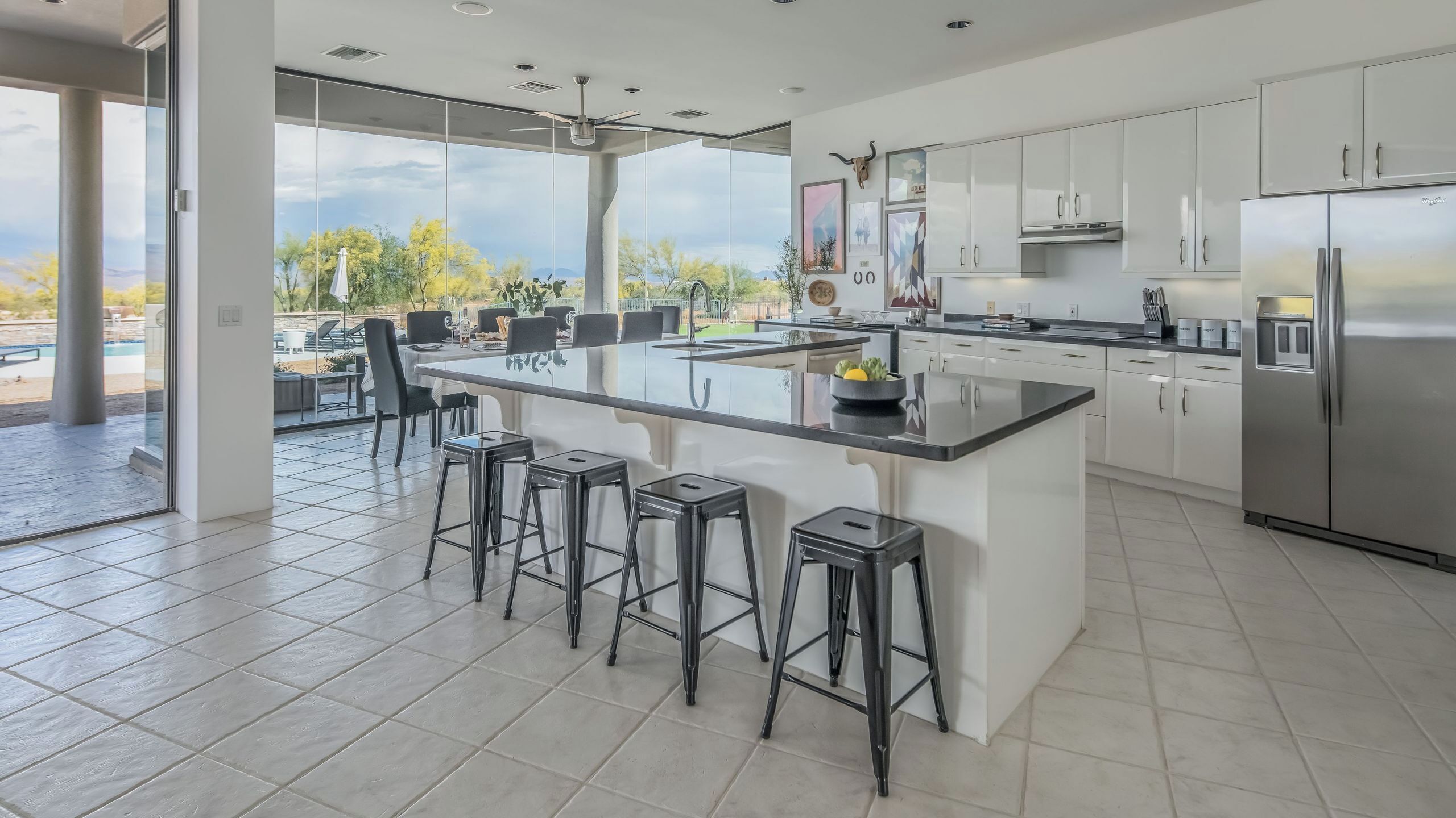 A modern kitchen with a large island, bar stools, stainless steel appliances, and a view of the outdoors.