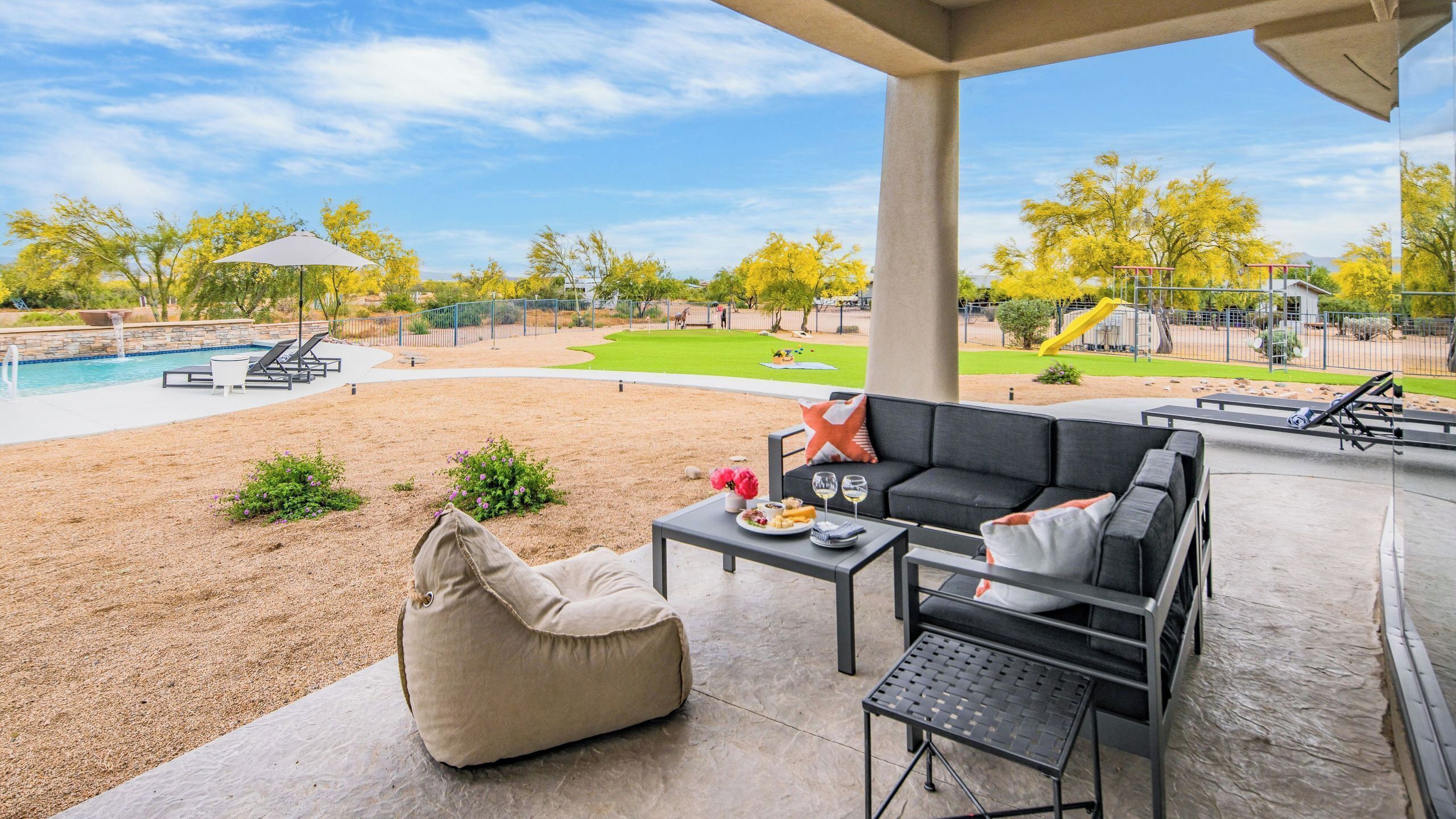 An outdoor patio area with a pool, a grassy lawn, and a playground in the background.