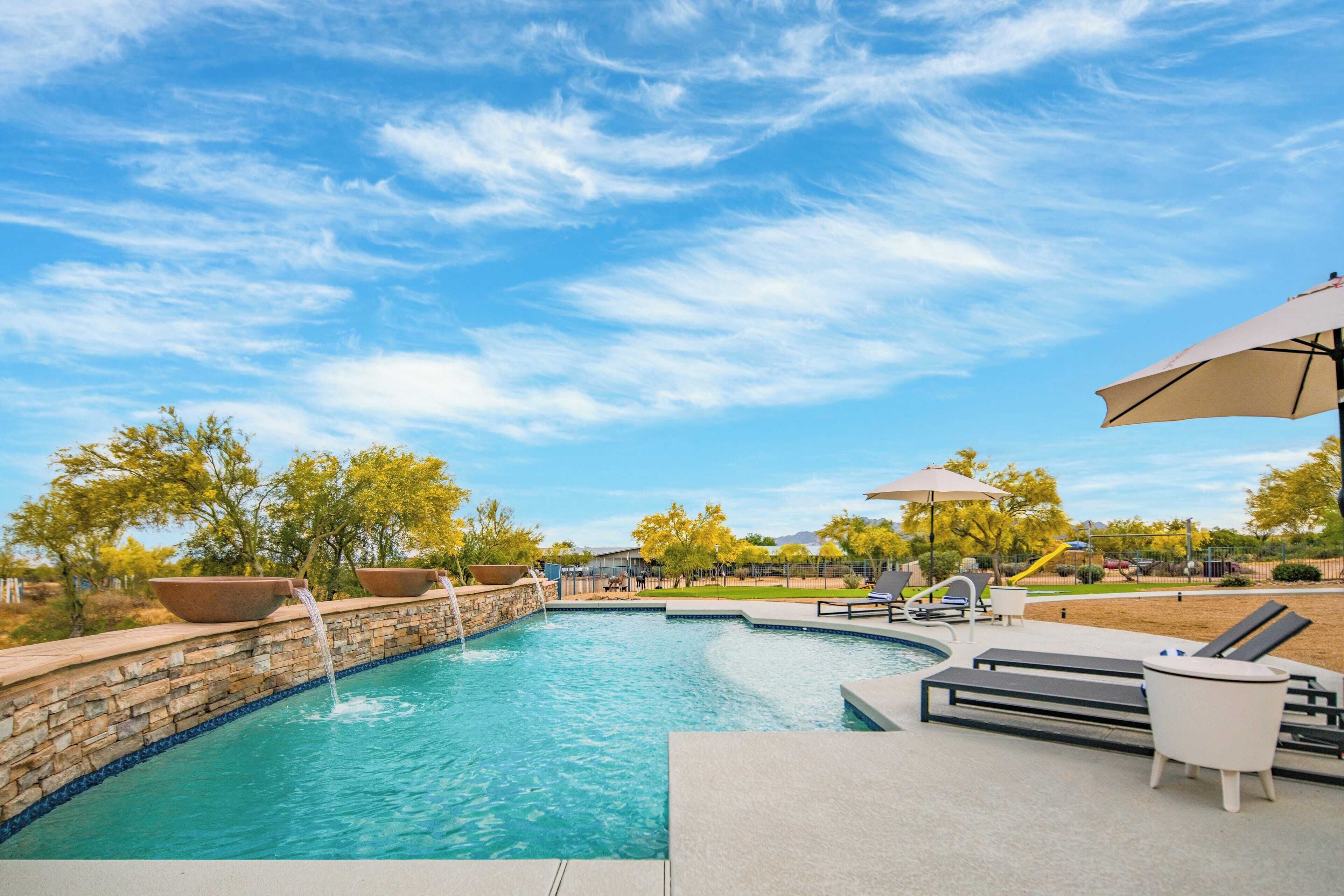 A swimming pool with a stone wall, lounge chairs, and umbrellas.