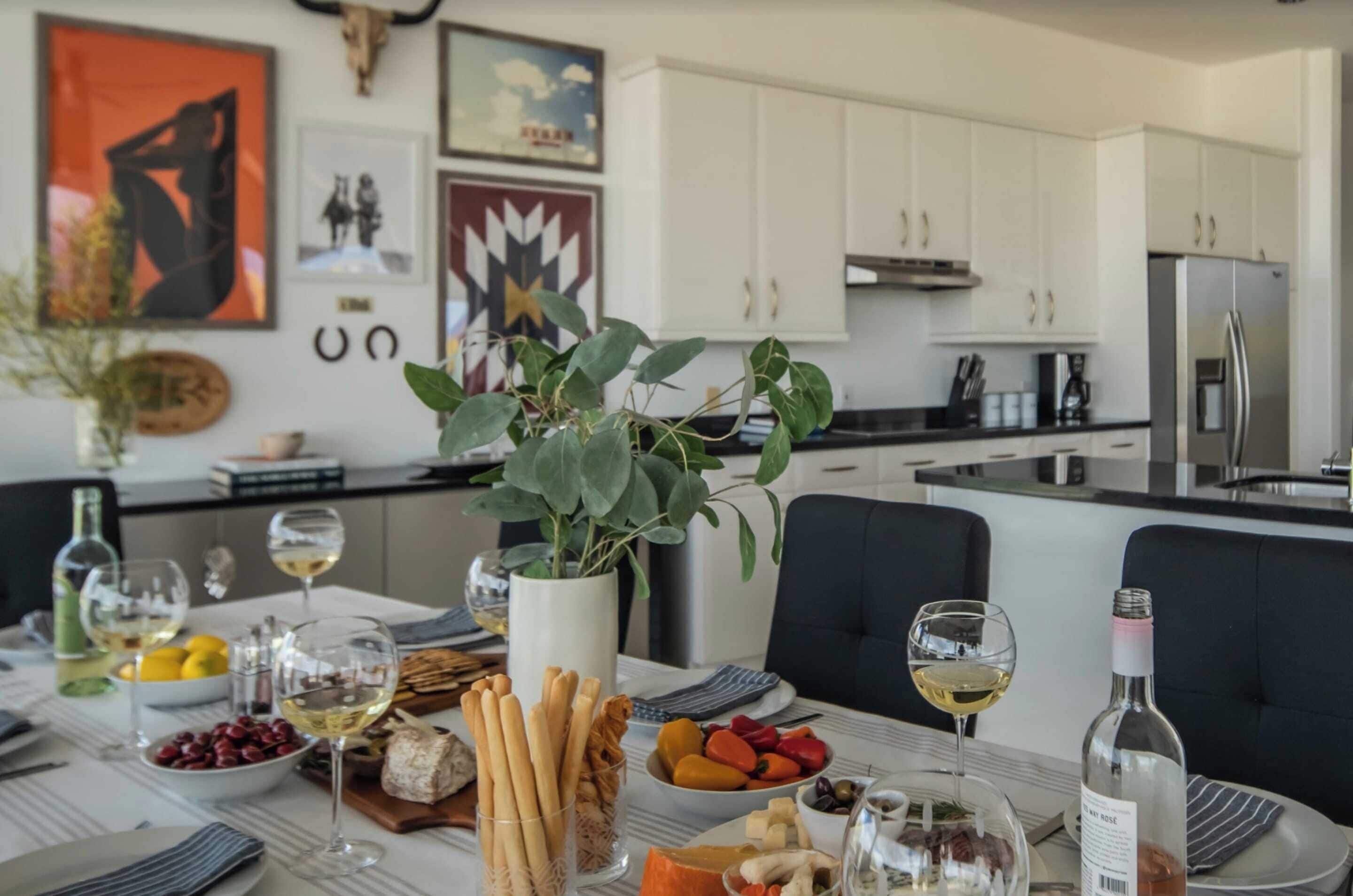 Una cocina moderna con armarios blancos, un refrigerador de acero inoxidable y un comedor con una mesa dispuesta para una comida.