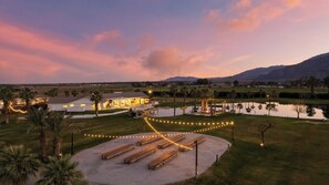 Un complejo turístico con un amplio comedor al aire libre, una piscina y un edificio con luces colgantes.