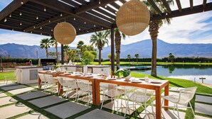 An outdoor patio with a wooden table and chairs, a grill, and a view of mountains and a lake. - 40-acre Estate, Priv Lake, Tennis, Golf Green, Soccer Buena Vista by Avantstay (Thermal)