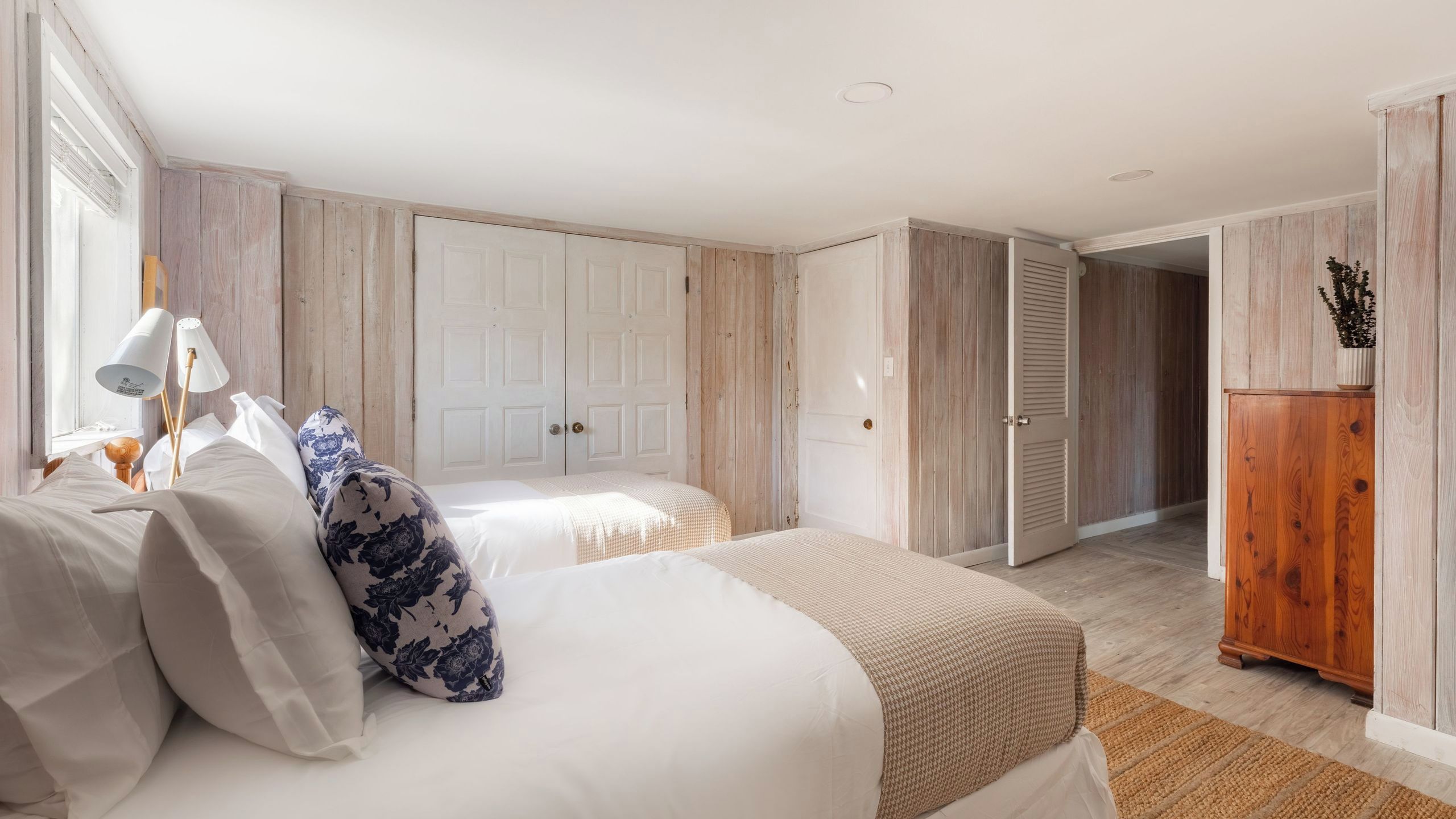 A bedroom with two beds, a wooden wardrobe, and a door leading to another room.