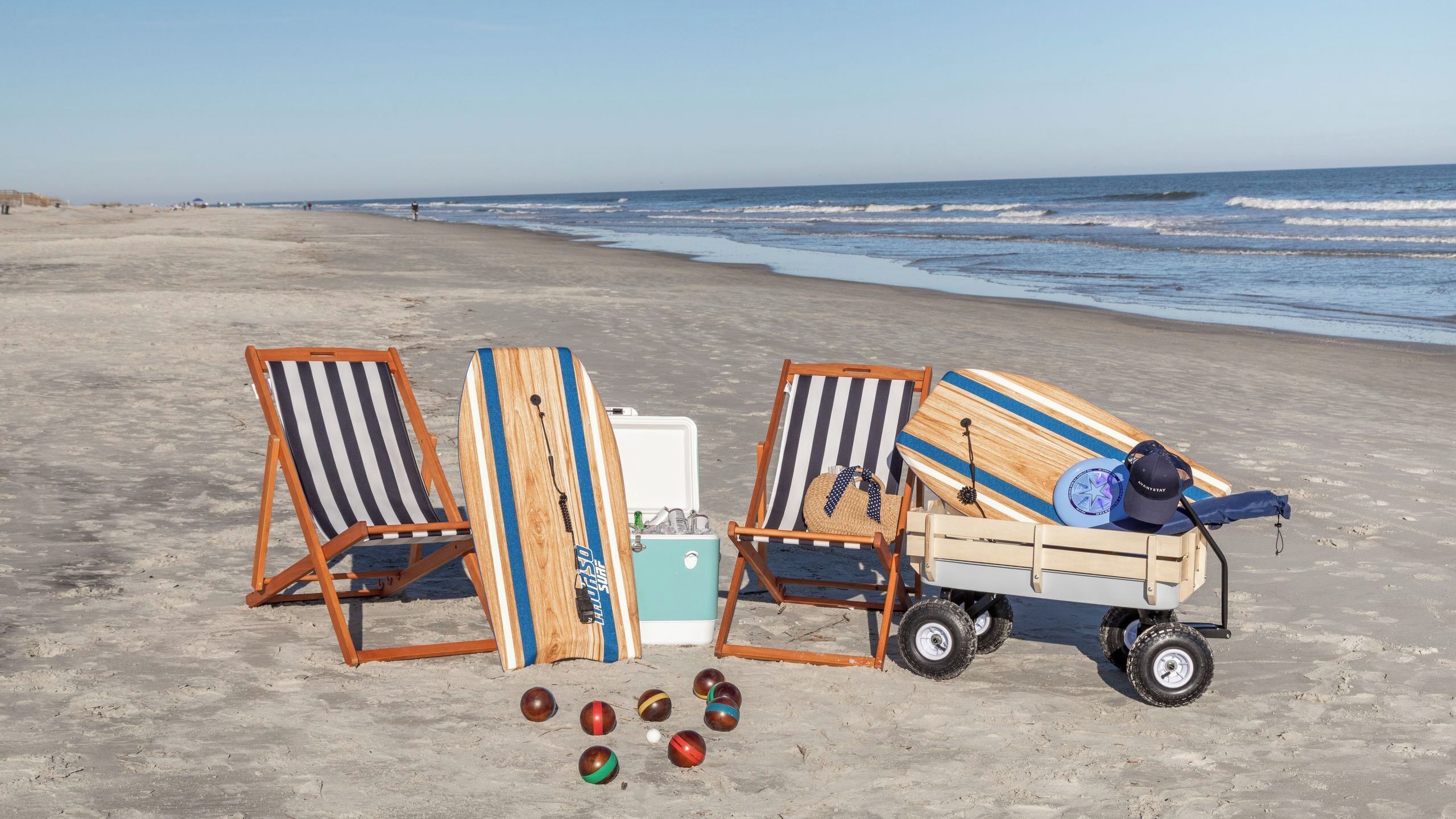 A beach scene with beach chairs, a cooler, a cart, and beach balls.