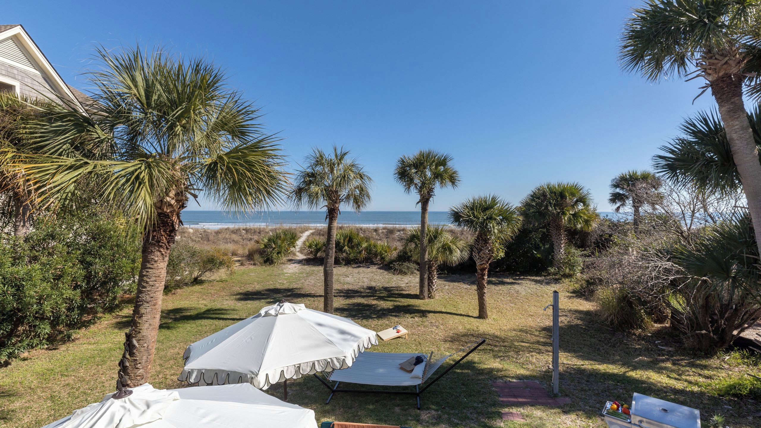 A backyard with a hammock, a white umbrella, and a view of the ocean.