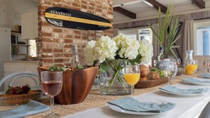 A breakfast setting with a brick wall, a sign reading 'AVANTSTAY,' and a table with plates, glasses, and a vase of flowers. - Sandpiper by Avantstay Gorgeous Beachside Home w/ Spacious Yard & Chic Design (Hilton Head Island)