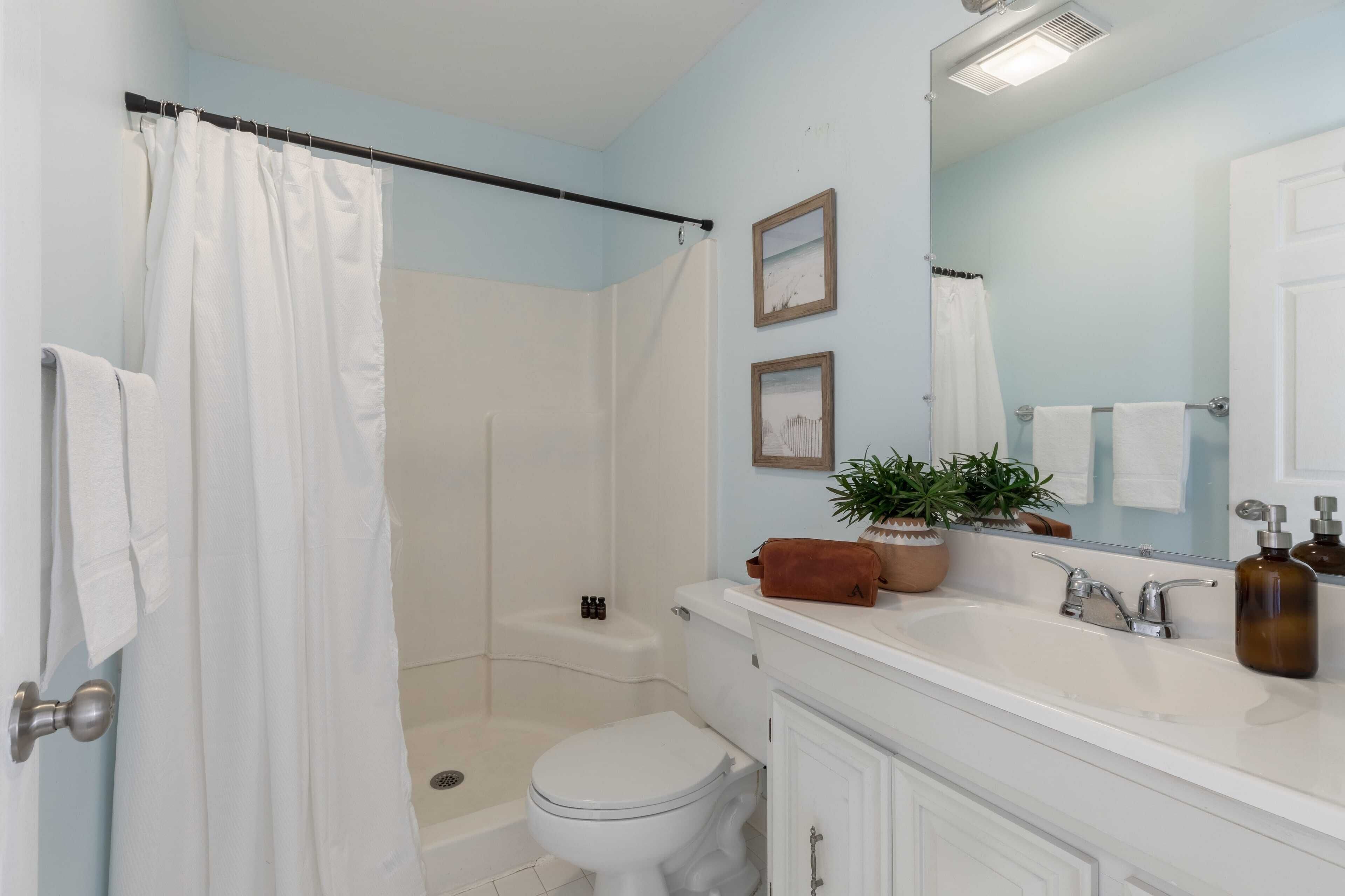 A bathroom with a shower curtain, toilet, sink, and mirror.