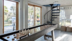 Una habitación amplia con una mesa de fútbolín de madera pulida, ventanas grandes que ofrecen vista a muebles de exterior y una escalera de caracol.