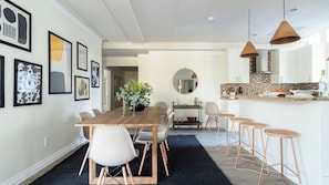Una cucina moderna con isola centrale, zona pranzo con tavolo e sedie in legno e un soggiorno con un grande specchio e opere d'arte alle pareti.