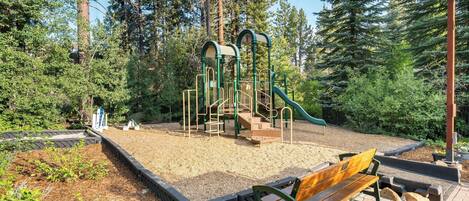 A playground with a slide and climbing structures, surrounded by trees.