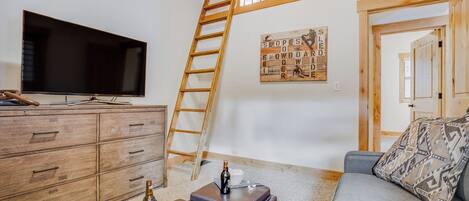 A living room with a TV, wooden dresser, a ladder, a board game, and a couch.