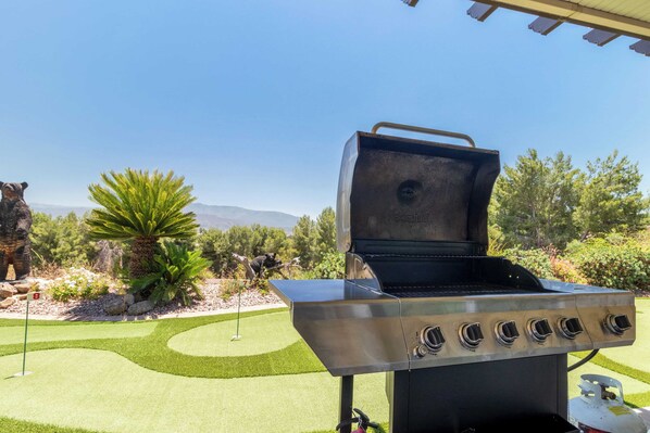Une terrasse avec un barbecue en acier inoxydable, un terrain de golf en arrière-plan et un ciel dégagé.