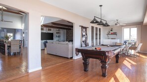 A spacious living area with a pool table, a dining area, and a kitchen visible through an archway. - Lighthouse by Avantstay Beachfront View Home w/ Pool Table & Ping Pong (Folly Beach)